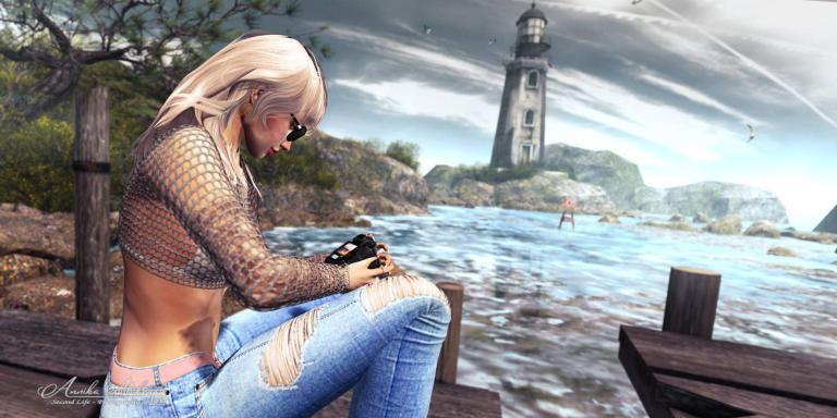 Annika Mohegan in Netzpullover und zerrissenen Jeans sitzt mit Kamera auf einem Steg vor einem Leuchtturm, Frogmore Cottage in Second Life